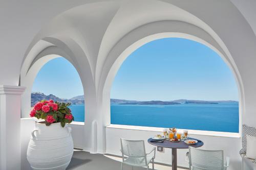 a room with a table and a view of the ocean at Katikies Santorini - The Leading Hotels Of The World in Oia