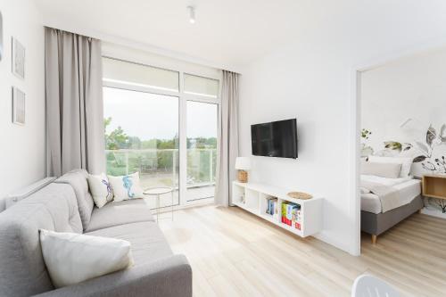 Una sala de estar blanca con un sofá y un televisor. en Apartament Perłowy z Basenem Letnim by HolidaySun, en Sianożęty