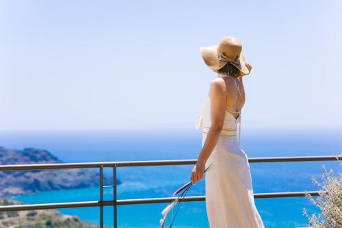 een vrouw in een witte jurk en hoed die naar de oceaan kijkt bij Villa Stella Suites in Plakias