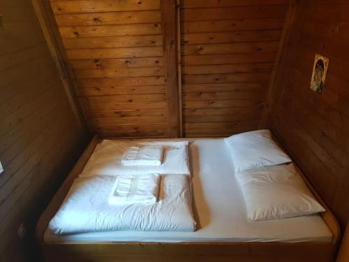 Bett in einem Holzzimmer mit weißer Bettwäsche und Kissen in der Unterkunft Rustical cottage with indoor fireplace in Sodražica