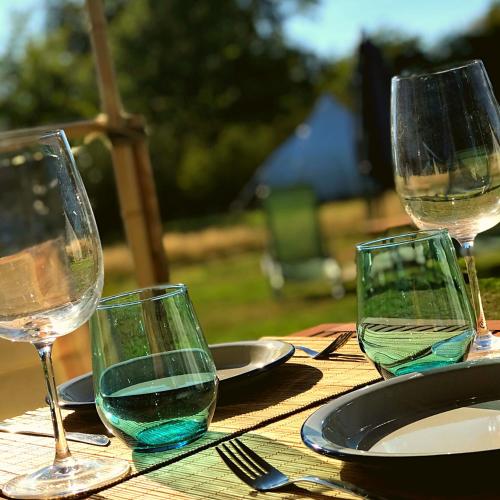 a table with three wine glasses and plates on it at La Prairie Étoilée Luxury Glamping - Adults Only in Crozon-sur-Vauvre