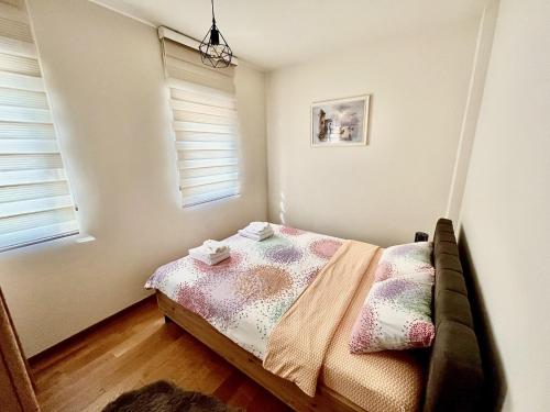 a small bedroom with a bed and two windows at Fides Stylish Apartments Tivat with Pool in Tivat