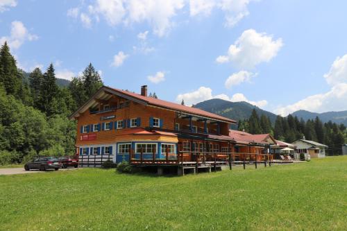 ein großes Holzgebäude auf einem Feld mit einem Auto vor der Tür in der Unterkunft Schelpenalp Berghotel Balderschwang in Balderschwang