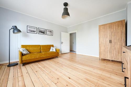 een woonkamer met een gele bank en houten vloeren bij Apartament Drewno i Biel 54 M2 in Olsztyn
