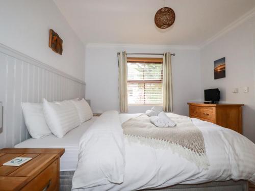 a white bedroom with a bed and a window at The Dunes in Crantock