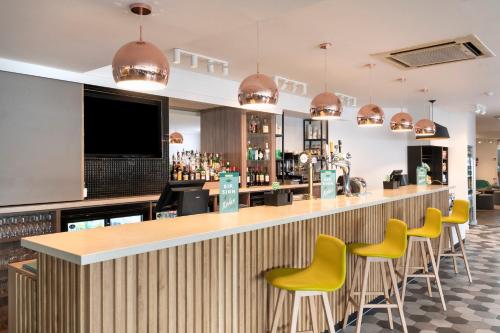 a bar with yellow bar stools in a restaurant at Holiday Inn Norwich, Ipswich Road by IHG in Norwich