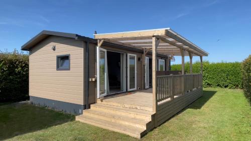 a tiny house with a deck on the grass at Chalet Boerenbries - Heerlijk chalet met overkapt terras en 2 slaapkamers - max 4 pers - 3 km van Noordzee - locatie op camping Moorhoek 5 in Rockanje