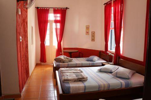 two beds in a room with red curtains and windows at Hotel Carvalho in Bragança Paulista