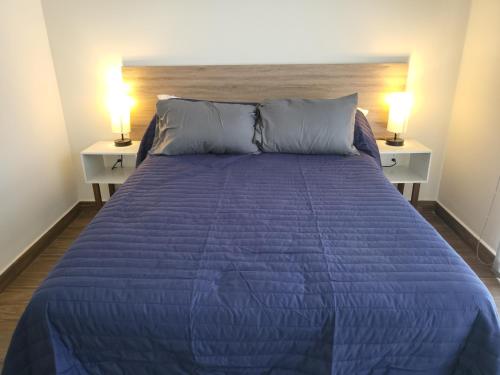 a bed with a blue comforter and two night stands at Departamento familiar o de negocios in Guadalajara