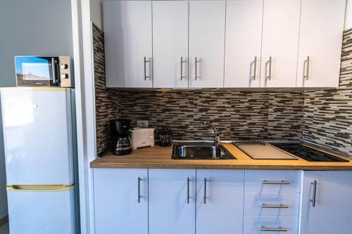 a kitchen with white cabinets and a sink and a refrigerator at Tindaya in Las Playas