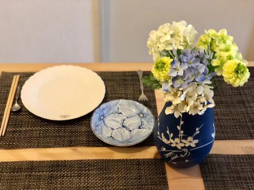 a table with two plates and a blue vase with flowers at Maison Etoile Room 705 - Vacation STAY 14807 in Nagoya