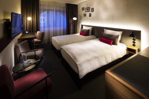 a hotel room with two beds and a chair at pentahotel Leuven in Leuven