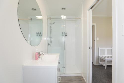 a white bathroom with a sink and a mirror at The Greenkeeper's Cottage in Rotorua