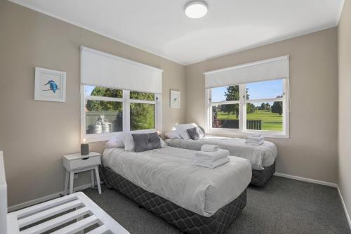 two beds in a room with two windows at The Greenkeeper's Cottage in Rotorua