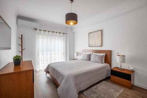 a white bedroom with a bed and a window at Porto Santo Apartment in Nazaré