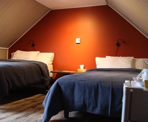 2 camas en una habitación con pared de color naranja en Chez Casimir en Matapedia