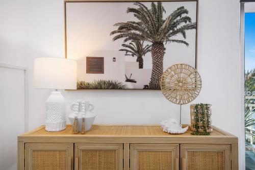 a dresser with a lamp and a palm tree picture on the wall at Ocean Spray 7 in Coffs Harbour
