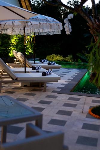 a row of lounge chairs and umbrellas next to a pool at Adepa Resort in Canggu