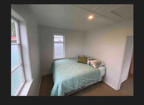 a small bedroom with a bed and two windows at Our Basic Bach - Mangakino in Mangakino