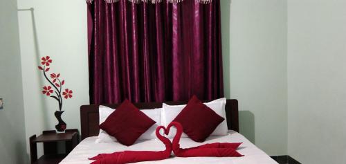 a bed with red pillows in front of a red curtain at Acharyaa Homestay in Tiruchchirāppalli