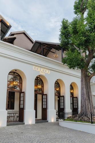 a white building with a tree in front of it at Coucou Hotel in Chiang Mai