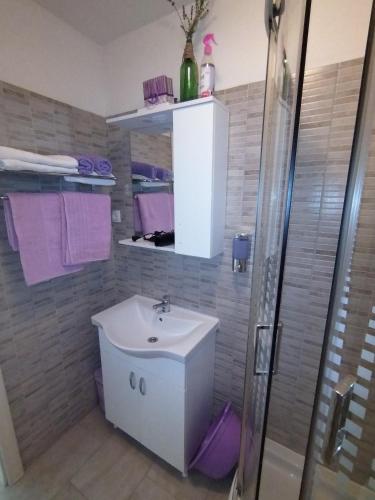 a bathroom with a sink and a shower with purple towels at Apartmani Kulin 2 in Kaštela