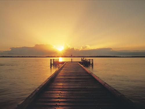 a dock on a lake with the sunset in the background at Quaint, Charming Pumicestone Cottage - Beach Charm - ZA7 in Golden Beach