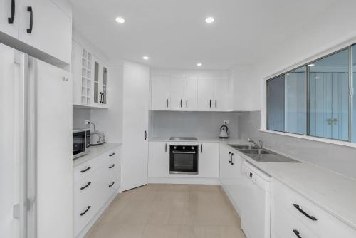 a white kitchen with white cabinets and a window at Endeavour Holiday House Clifton Beach in Clifton Beach