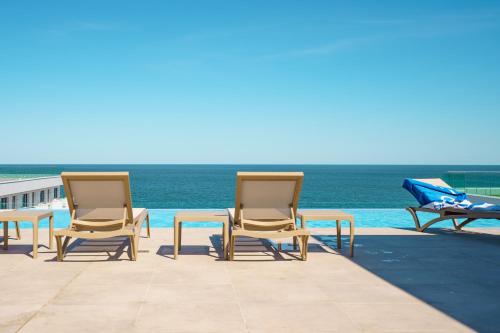 um grupo de cadeiras e uma mesa junto ao oceano em Royale Sundance 305 Infinity Beach Pool & Spa Mamaia Nord em Mamaia Nord – Năvodari