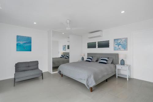 a white bedroom with a bed and a chair at Endeavour Holiday House Clifton Beach in Clifton Beach
