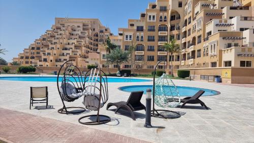 a pool with chairs and a table in front of a building at Luxury see view studio Al Marjan in Ras al Khaimah