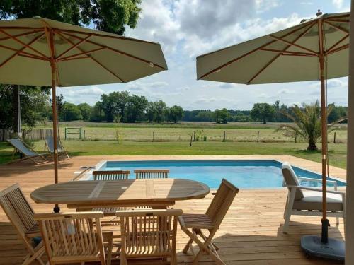 a table and chairs with umbrellas next to a pool at Maison neuve avec piscine chauffée, 4 kms de Contis plage in Saint-Julien-en-Born