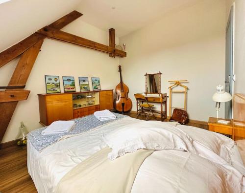 a bedroom with a large white bed and a guitar at La Cour Verte : Chaleureuse grange réhabilitée in Montépilloy