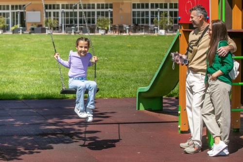 a little girl sitting on a swing in a playground at Gotthard Therme Hotel & Conference in Szentgotthárd