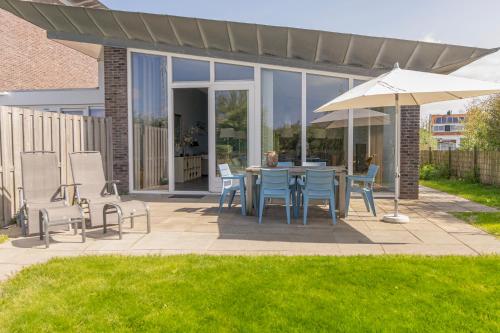 eine Terrasse mit einem Tisch, Stühlen und einem Sonnenschirm in der Unterkunft Beachlife 9 in Callantsoog