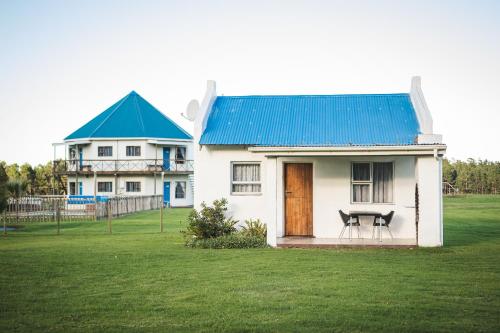Casa blanca con techo azul y mesa en la parte delantera en Tsitsikamma Cottages, en Witelsbos