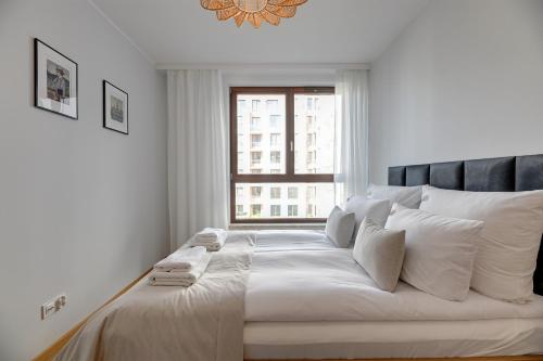 a white bedroom with a large bed with a window at Downtown Apartments Garnizon in Gdańsk