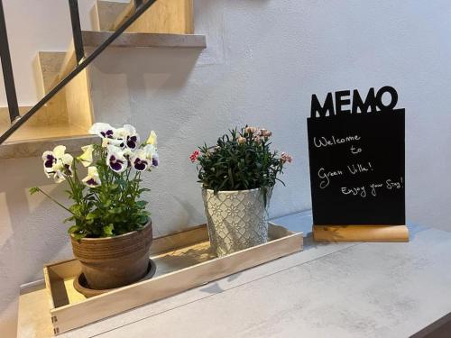 due vasi di fiori su uno scaffale con un cartello di Green Villa - CityDoor a Lacchiarella