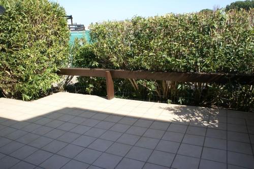 un banc en bois assis sur un trottoir à côté d'une haie dans l'établissement Appartement cabine 908 Tennis Village 6 personnes, au Cap d'Agde