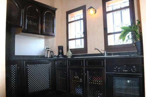 eine Küche mit schwarzen Schränken, einem Waschbecken und 2 Fenstern in der Unterkunft Chambre Merzouga, Riad 8 au village naturiste Couple only in Cap d'Agde