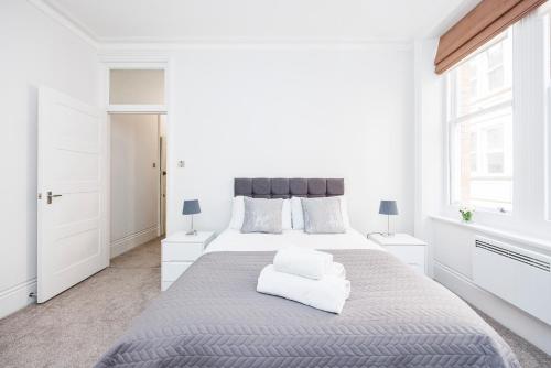 a white bedroom with a large bed and two windows at Leicester Square Apartment in London