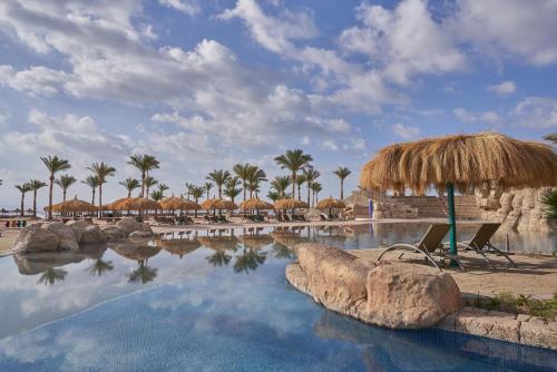 een zwembad van het resort met een rieten parasol en palmbomen bij The Bayview Taba Heights Resort in Taba