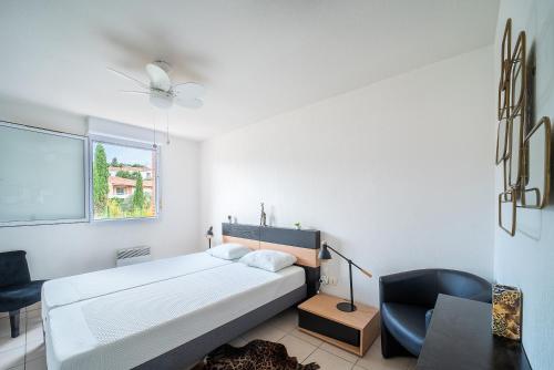 a white bedroom with a bed and a chair at La Casa de Cricri - Appartement climatisé in Perpignan