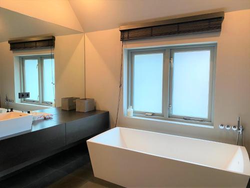 a bathroom with a large white tub and two windows at Studio het Strandhuis KA05 in Vlissingen