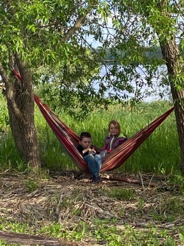 two children sitting in a hammock under a tree at Senči in Koknese