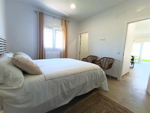 1 dormitorio con 1 cama blanca, ventana y sillas en Villas Florida, en Conil de la Frontera