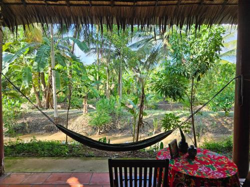 a hammock in a room with a table and a view of a forest at Ba Danh Homestay & Kitchen - Ben Tre Mekong in Ben Tre