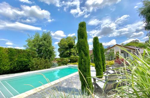 una piscina con cipreses frente a una casa en La Maison de Manolie en Courcelles-Sapicourt