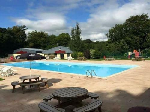 a large swimming pool with a picnic table and benches at Stunning 3 Bed Riverside Cabin in Snowdonia in Caeathro