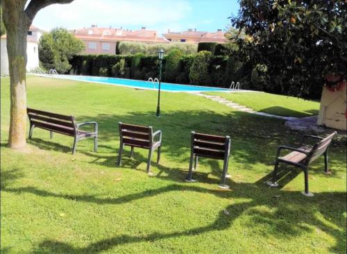 tres bancos de parque sentados en el césped junto a un árbol en Apartamento en Platja Sant Pol S'agaro con pisicina y jardin (playa - centro), en Sant Feliu de Guíxols